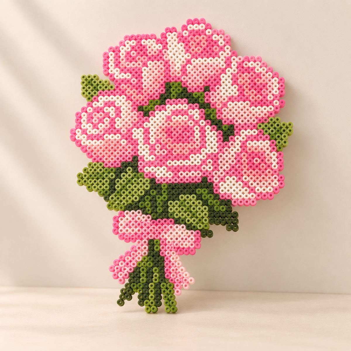 Pink rose bouquet fuse bead artwork with green leaves and a pink bow on a cream background.