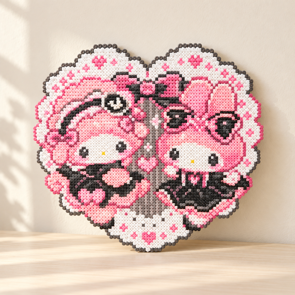 Pink heart fuse bead artwork with two pink-hooded characters displayed on a cream table in soft daylight.